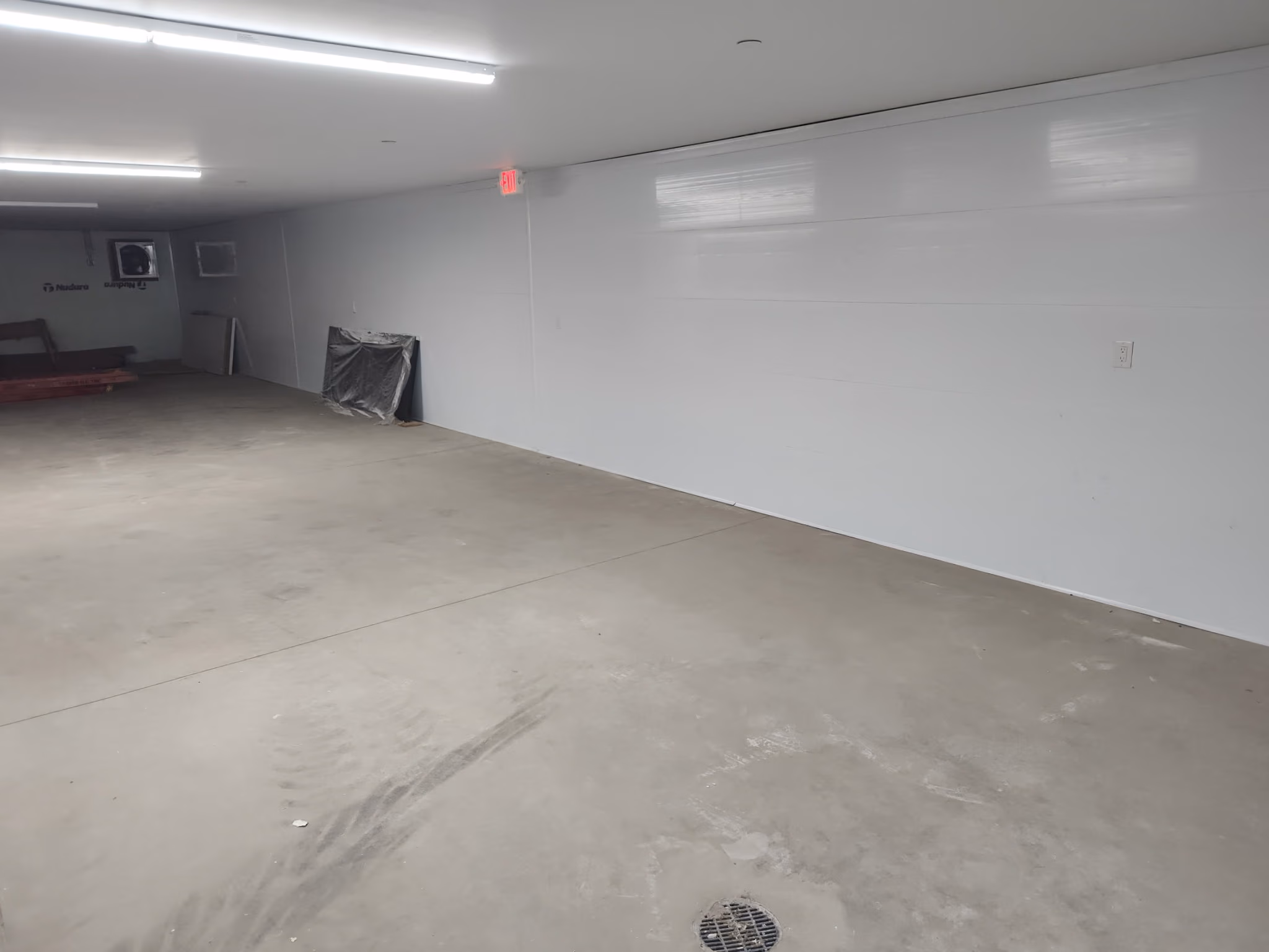 Empty room with smooth concrete floor, white walls, ceiling lights, and a floor drain near the foreground.