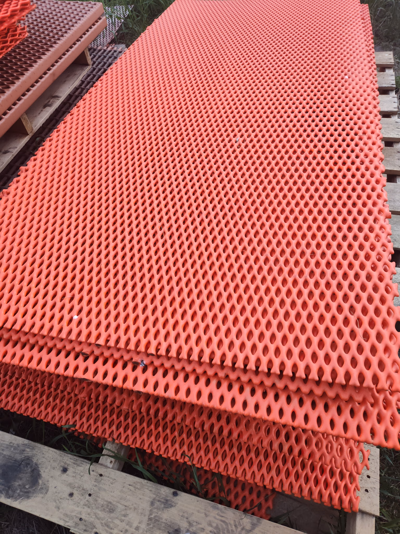 Stack of orange perforated plastic safety mats on wooden pallets outdoors.