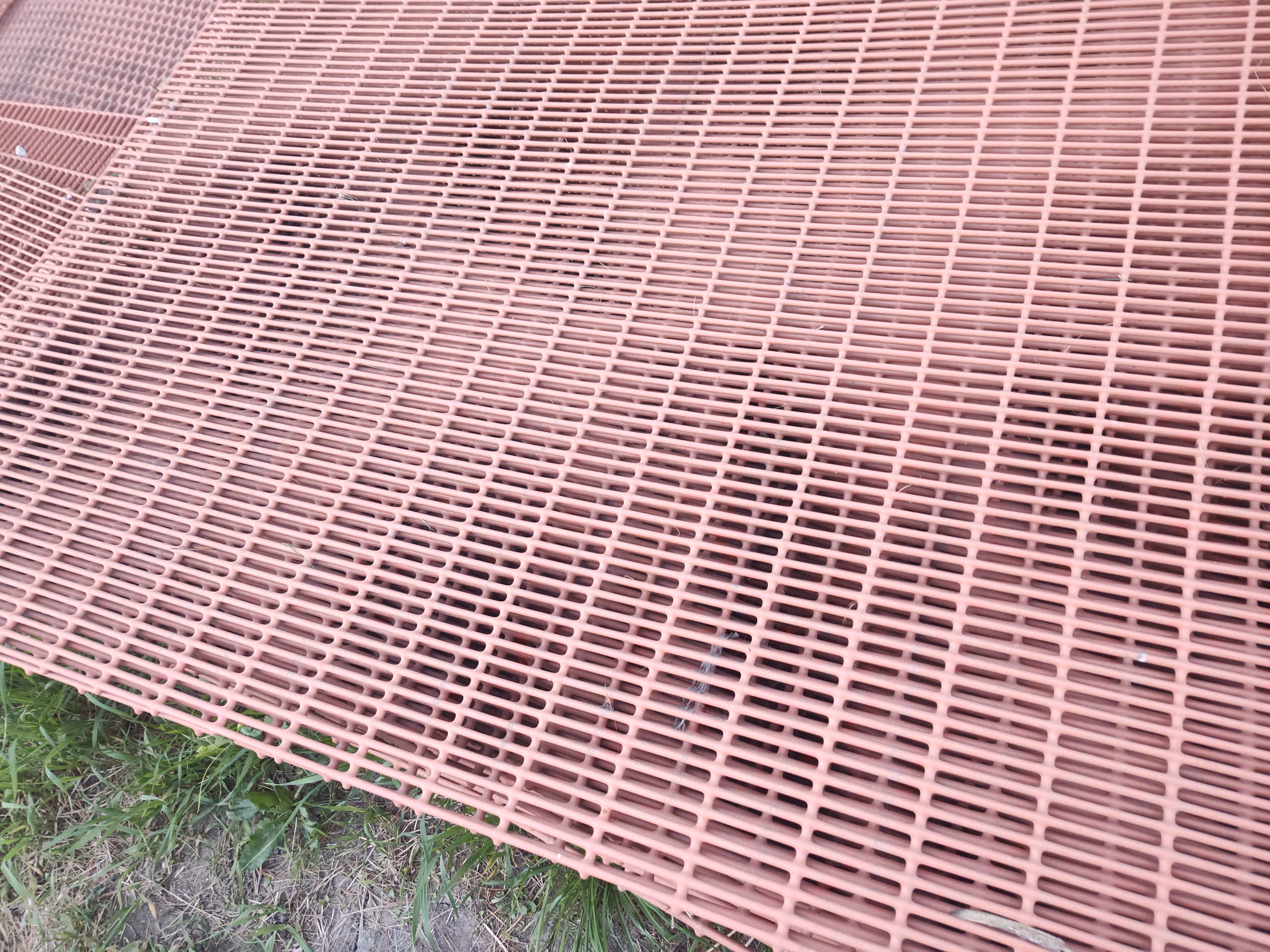 Close-up of overlapping pink plastic grates on grass and dirt ground outdoors.