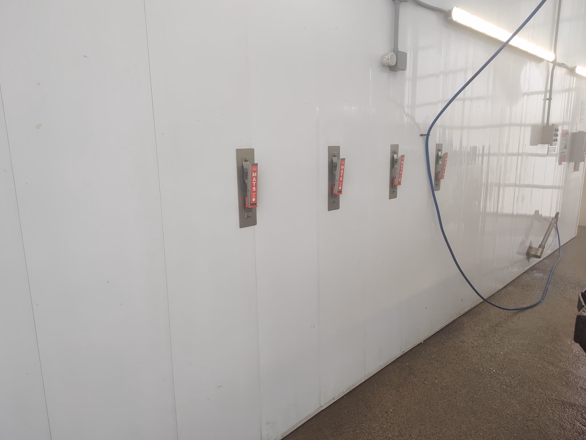 White industrial wall with four red emergency handles and a hanging blue hose in a utility room.